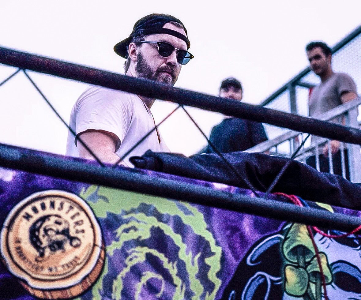 Person playing a turntable at a Moonsters NFT NYC music event with colorful equipment and a crowd in the background.