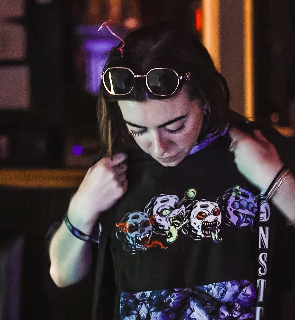 Female examining a black graphic crop top with colorful Moonsters designs in a dimly lit room at Manhattan NFT NYC event.