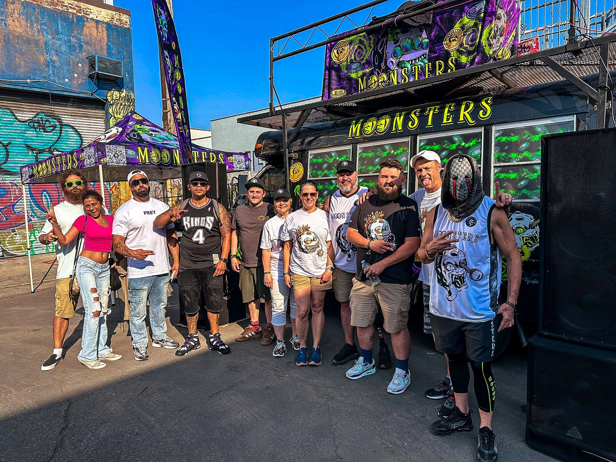 Group of people posing in front of a colorful Moonsters stage bus with at Brooklyn NFT NYC event.