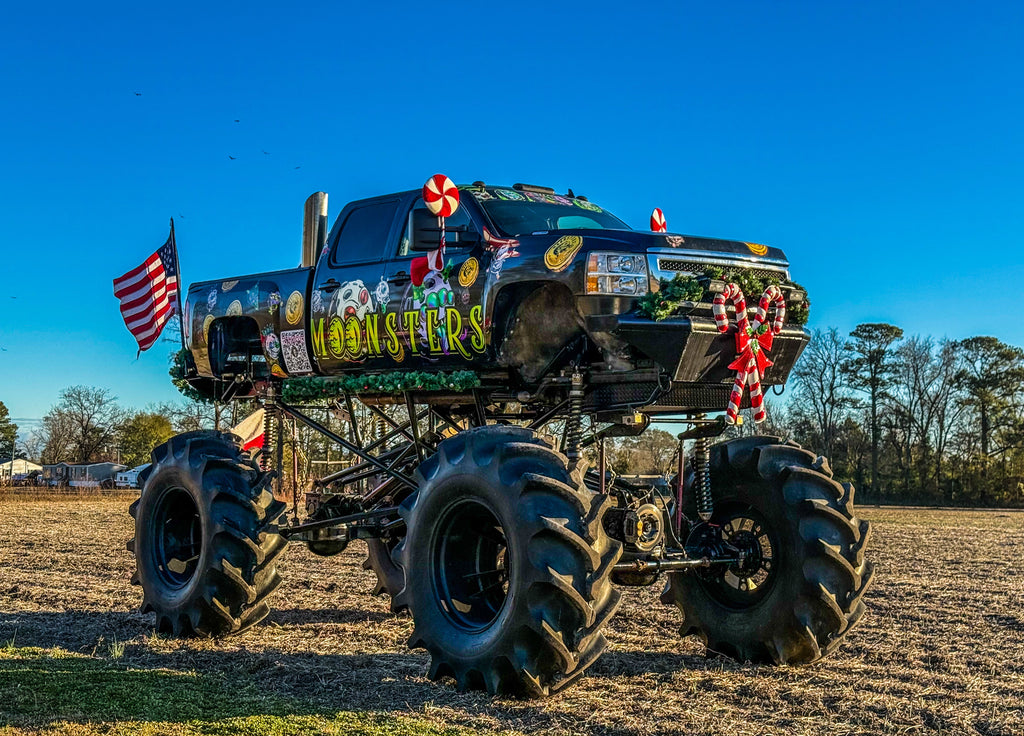 Moonsters monster truck with large wheels and festive christmas decorations in a field.