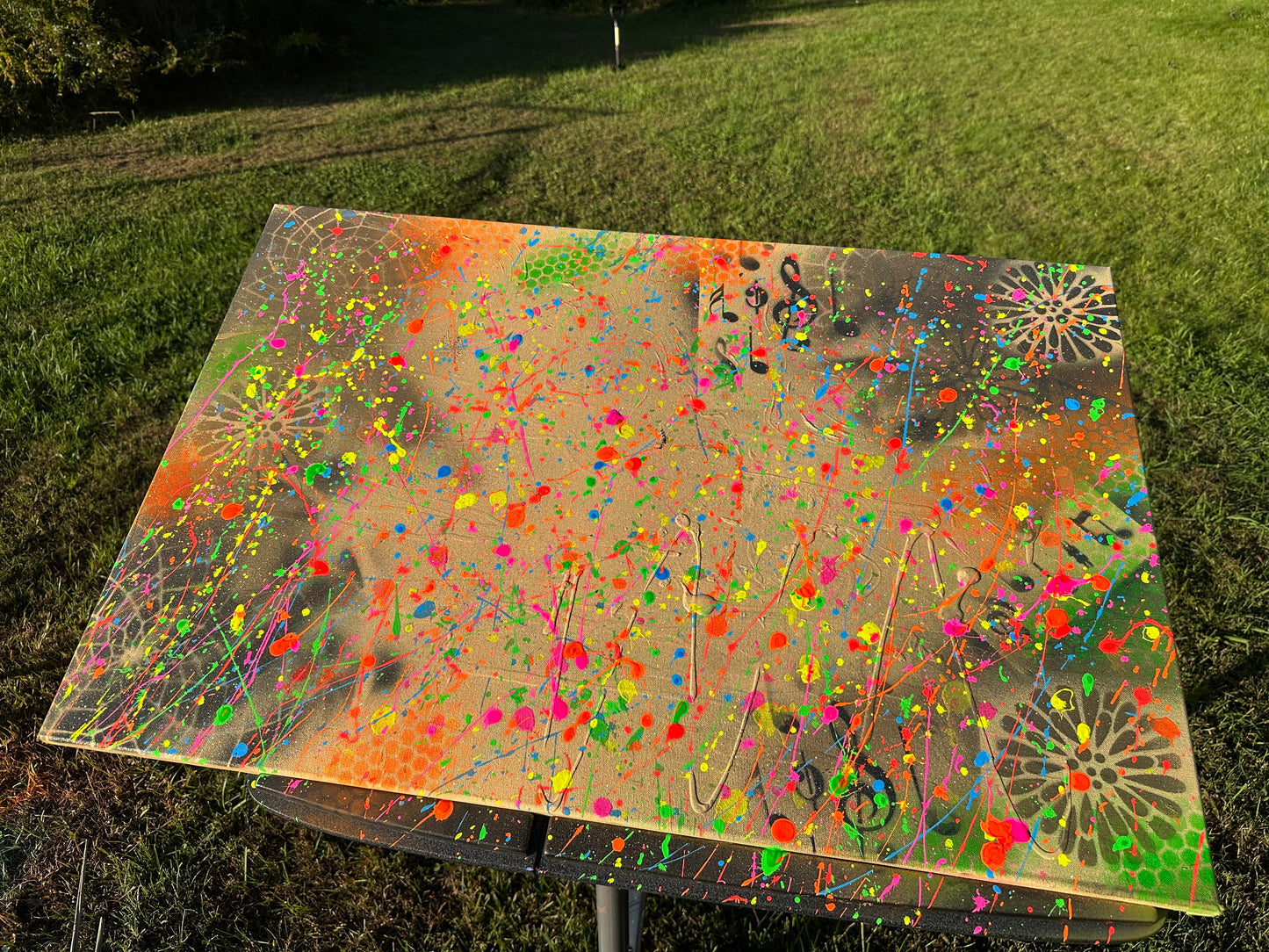 Rectangular artwork with neon splatter paint on brown canvas featuring vibrant pink, green, orange, and yellow accents.