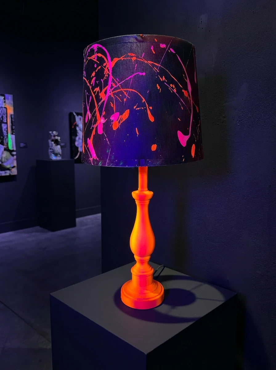 Table lamp with neon orange & pink base and dark shade splattered with bright pink and orange paint.