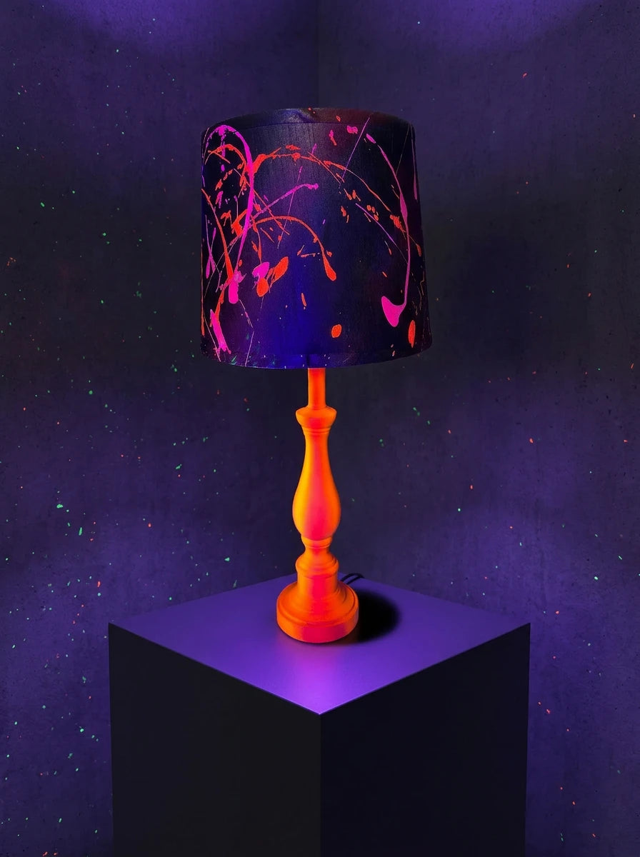 Table lamp with neon orange & pink base and black lampshade splattered with pink and orange paint.