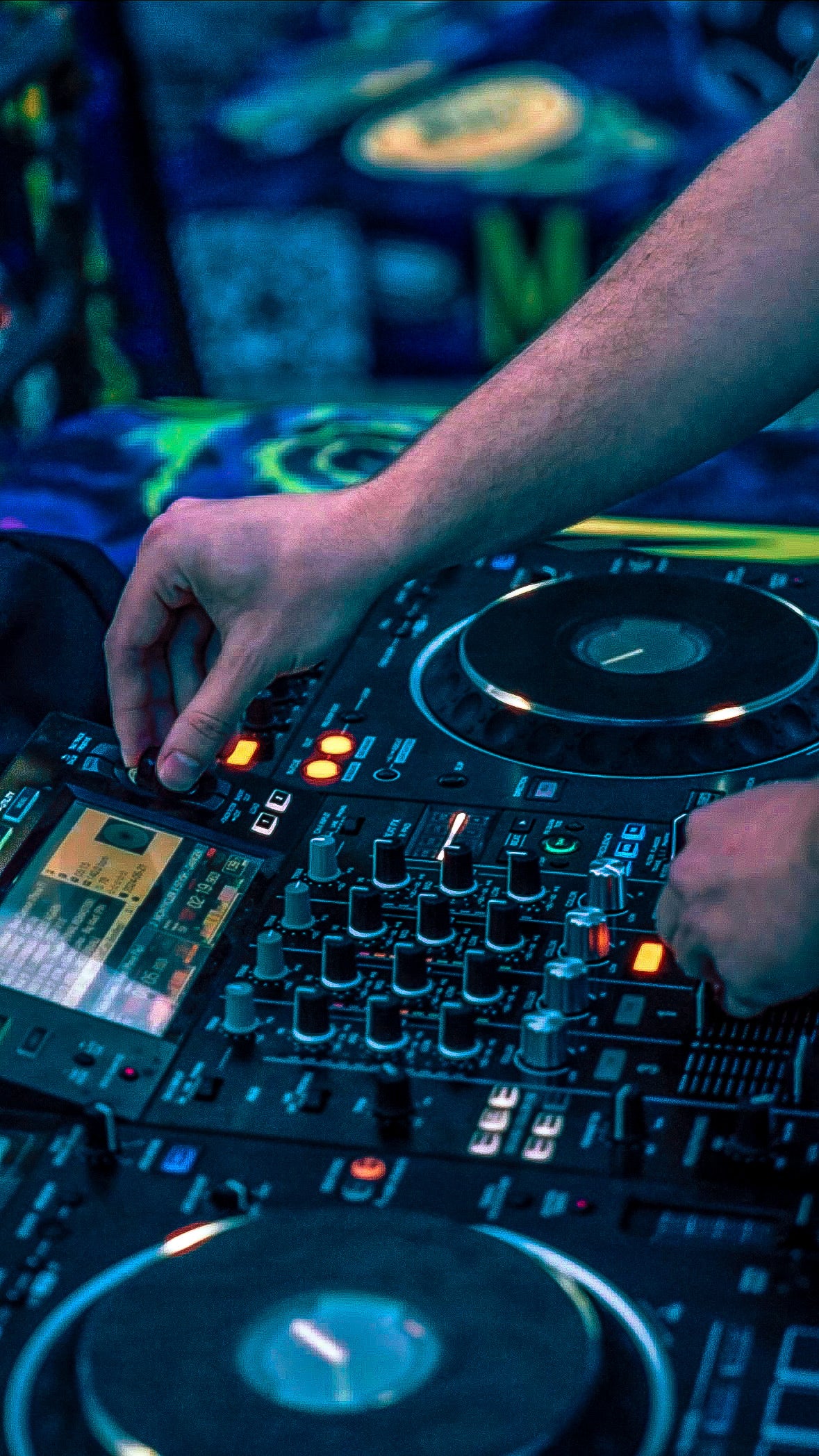 Close-up of hands operating a DJ mixer with neon lights in the background at Moonsters Brooklyn NFT NYC event.