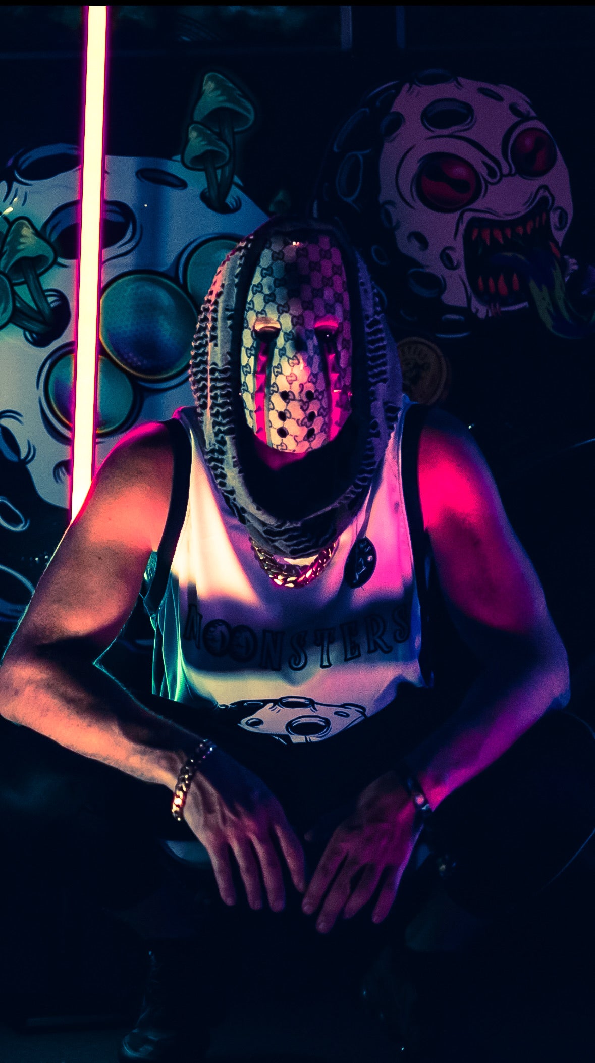 The Sol Saver wearing a Gucci ski mask and tank top in a dark setting with neon lights